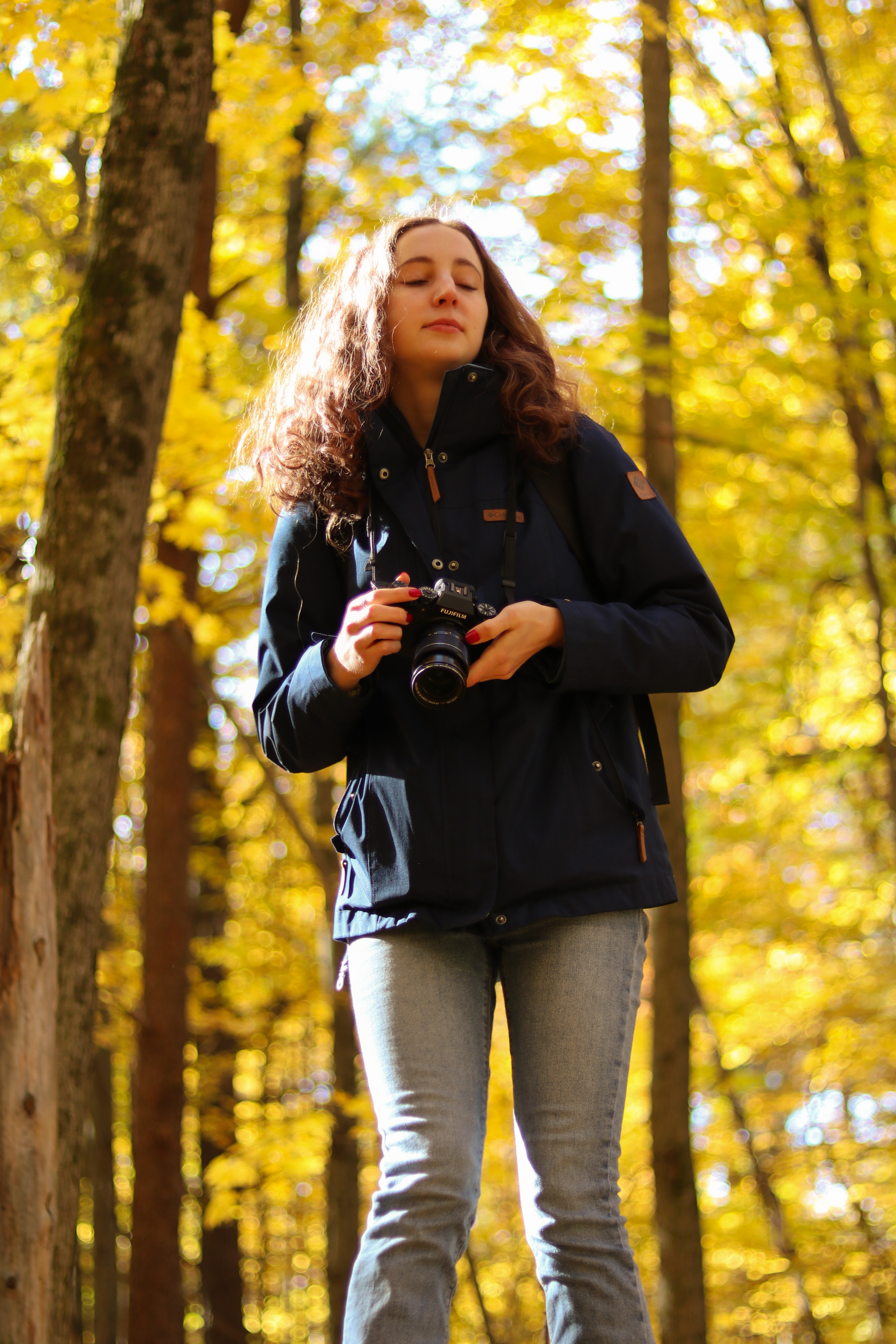 A candid photo of a girl posed in a forest, holding her camera